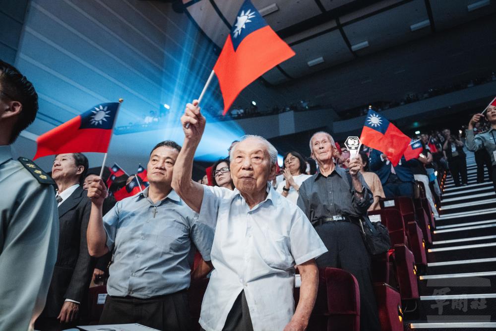 抗戰前輩於紀念音樂會上振臂揮舞手中國旗，展現愛國情懷與堅毅信念。（軍聞社記者陳彥樺攝）
