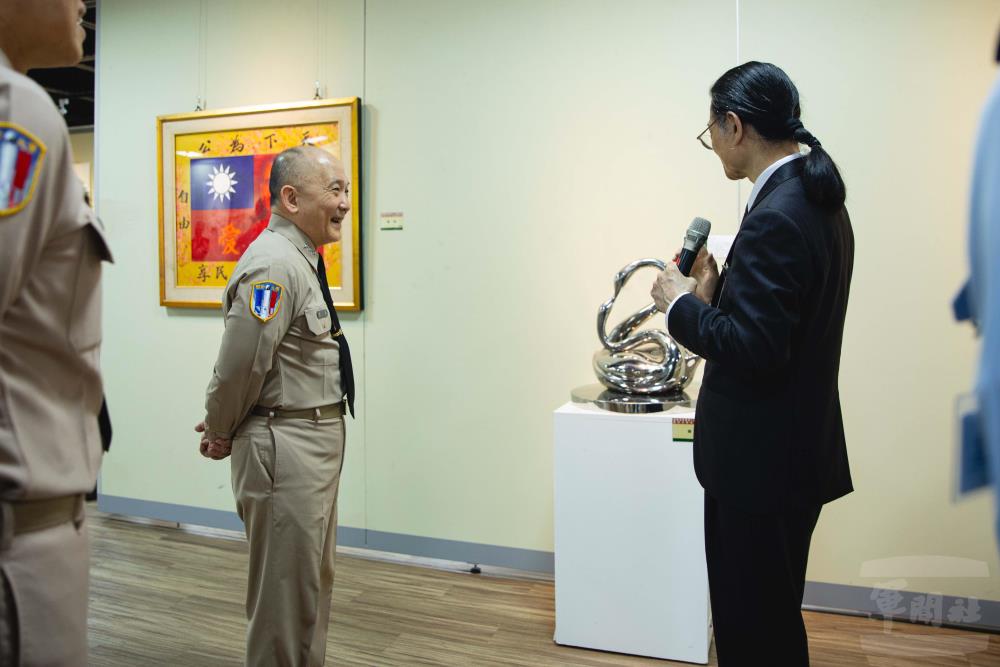 藝術家李寶龍介紹雕塑作品《韻》，透過流動曲線與循環造型，傳達自然、生命與環境共生理念。（軍聞社記者邱奕菖攝）
